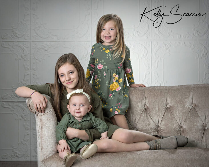 Studio portrait three little sisters together wearing green sitting on a couch