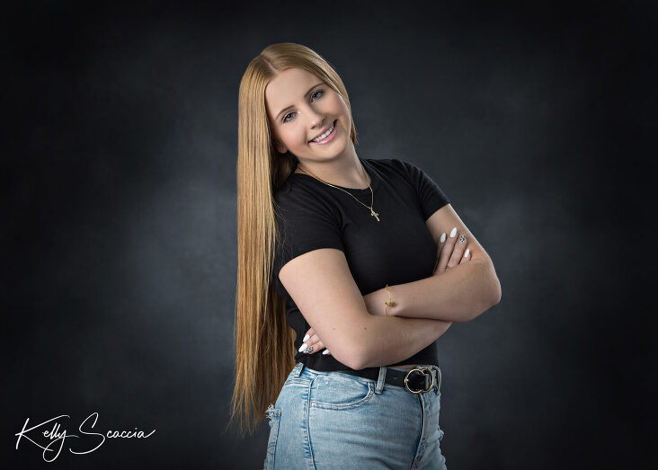 senior girl studio portrait long, red, straight hair, black shirt and jeans looking at you smiling