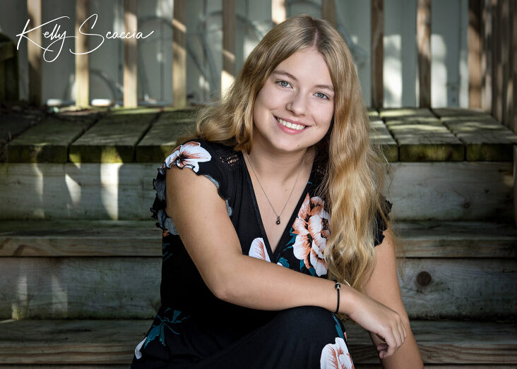 Outdoor portrait teenage girl wearing black, floral, long dress, long, blonde hair smiling looking at you