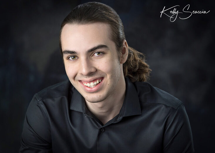 Studio senior guy portrait wearing a black button down shirt and jeans, looking at you, smiling