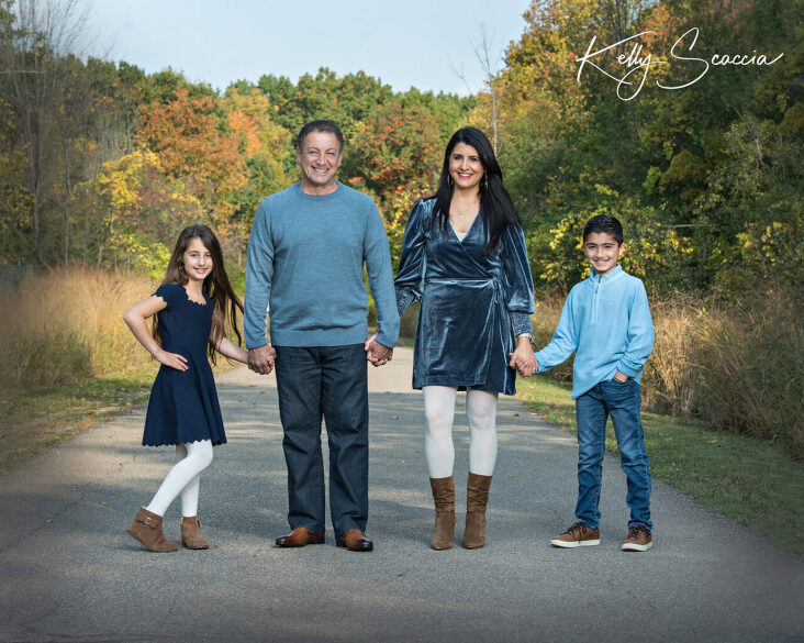 family of four outdoor fall portrait, all wearing blue clothing, smiling and looking at you, holding hands