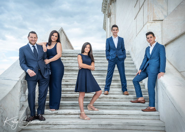 Outdoor DIA portrait family of five in blue formal clothing all have dark hair dark eyes standing on white marble steps posed