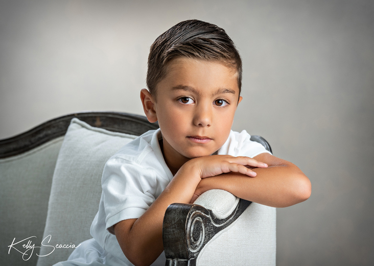 Studio little boy portrait in white shirt, looking at you, resting chin on hands