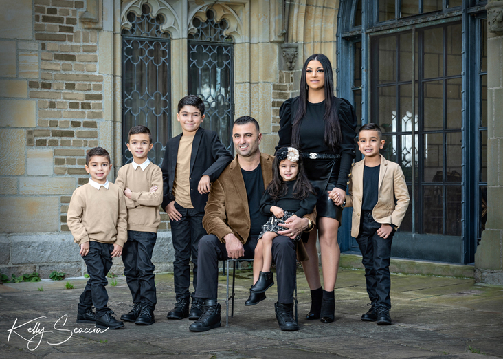 Outdoor family of seven portrait with mom wearing black and tan, all dark hair, dark eyes, looking at you smiling