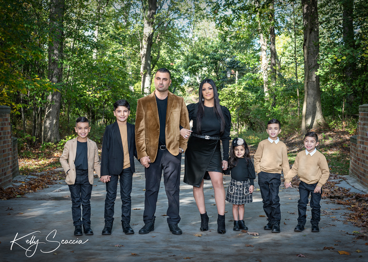 Outdoor family of seven portrait with mom wearing black and tan, all dark hair, dark eyes, looking at you smiling