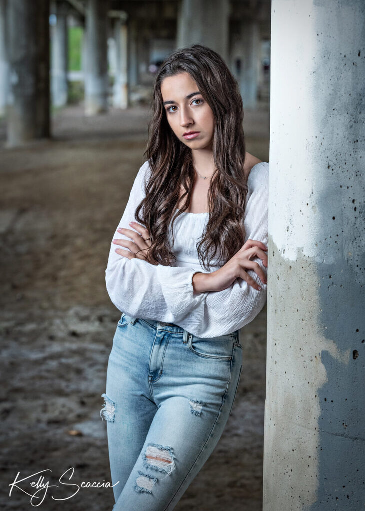 Outdoor senior girl portrait, long dark hair, dark eyes wearing white shirt and jeans, smiling, looking at you