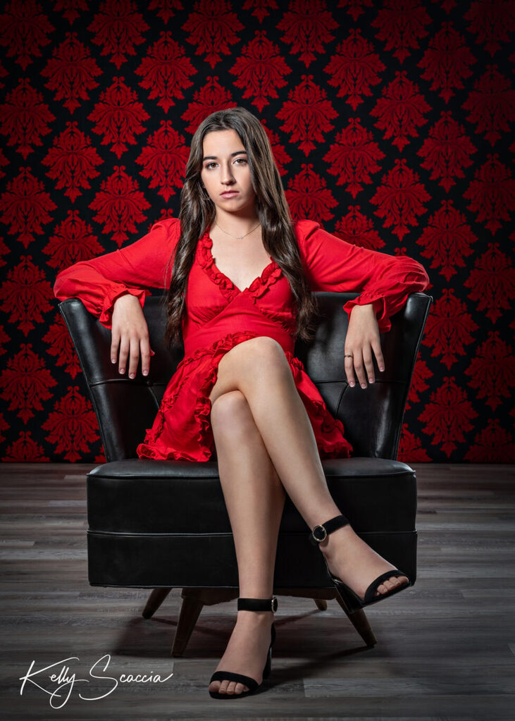 Studio senior girl portrait wearing red dress, long, brown hair, dark eyes, looking at you, serious expression