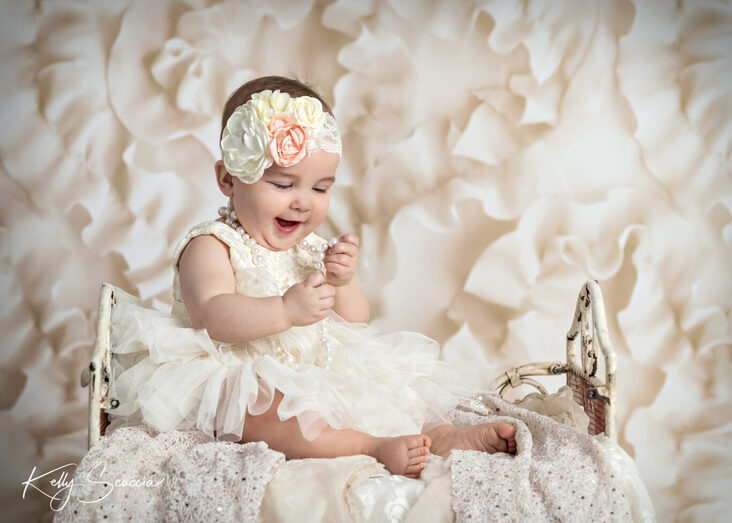 Studio baby girl one year birthday portrait, bright blue eyes, short hair, smiling, white tutu dress with white and peach flower headband