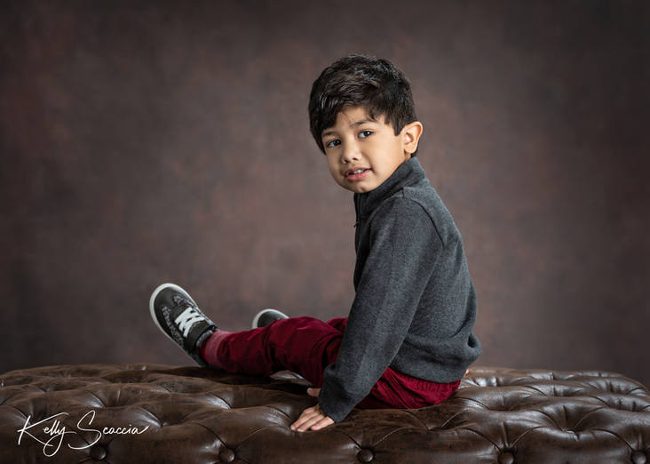Studio portrait little boy, dark hair and eyes, looking at you, smiling, wearing gray sweater