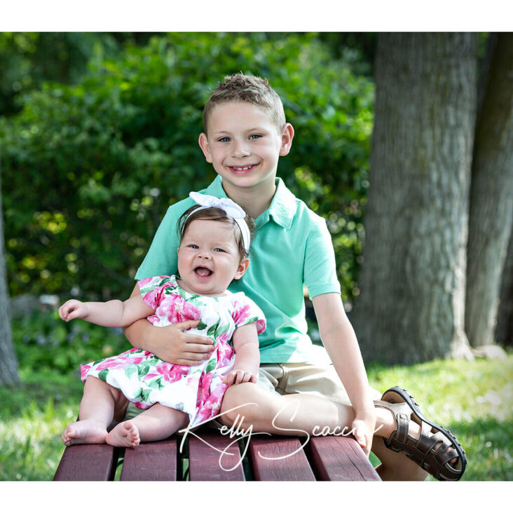 Outdoor portrait of little boy and baby girl sister sitting on a bench both smiling