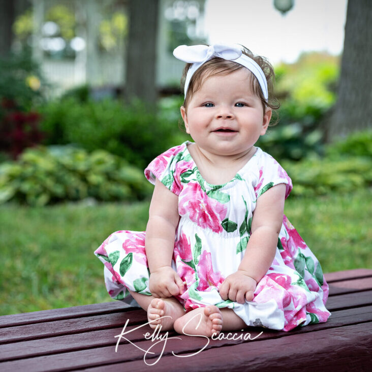 Outdoor portrait of baby girl wearing dress, smiling looking at you
