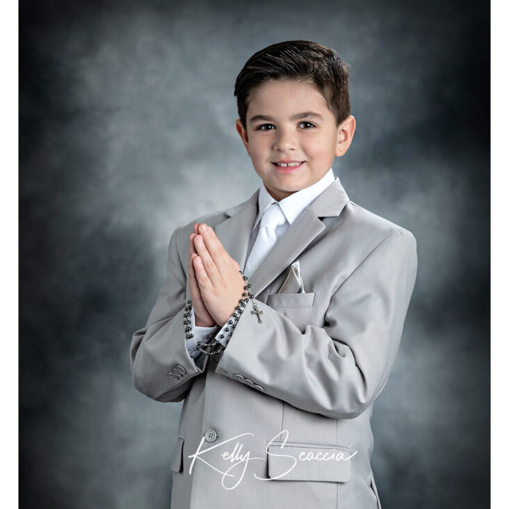 Communion boy studio portrait in light gray suit looking at you holding rosary