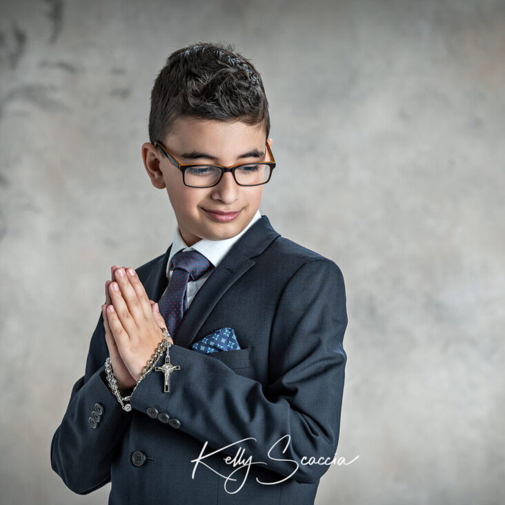 Studio communion boy in a dark suit portrait holding a rosary