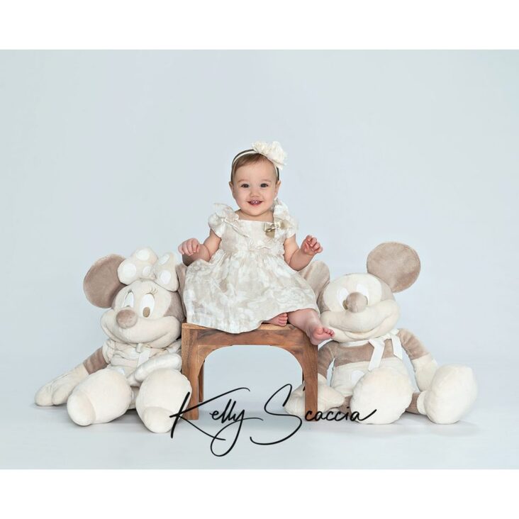 Studio portrait little baby, short brown hair, dark eyes, looking at you, smiling, wearing cream dress with a cream bow in her hair