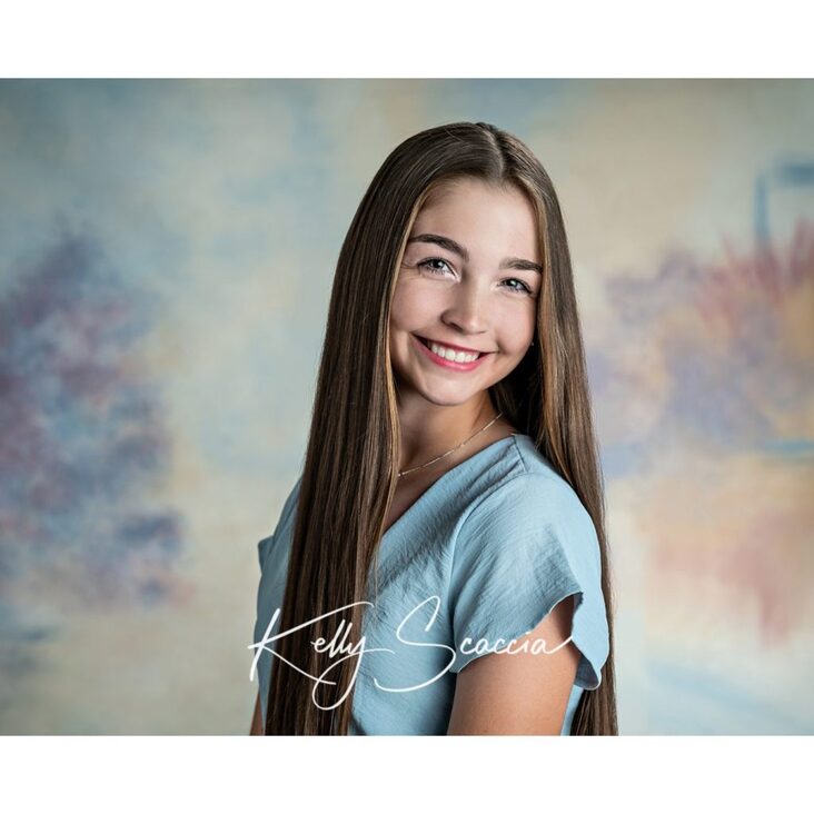 Studio high school senior girl portrait with long, dark brown hair, dark eyes, looking at you, wearing blue short dress, smiling