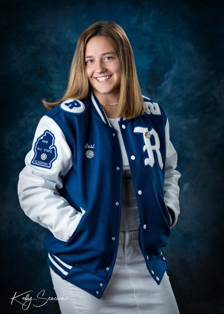 High School senior girl in varsity jacket in studio smiling