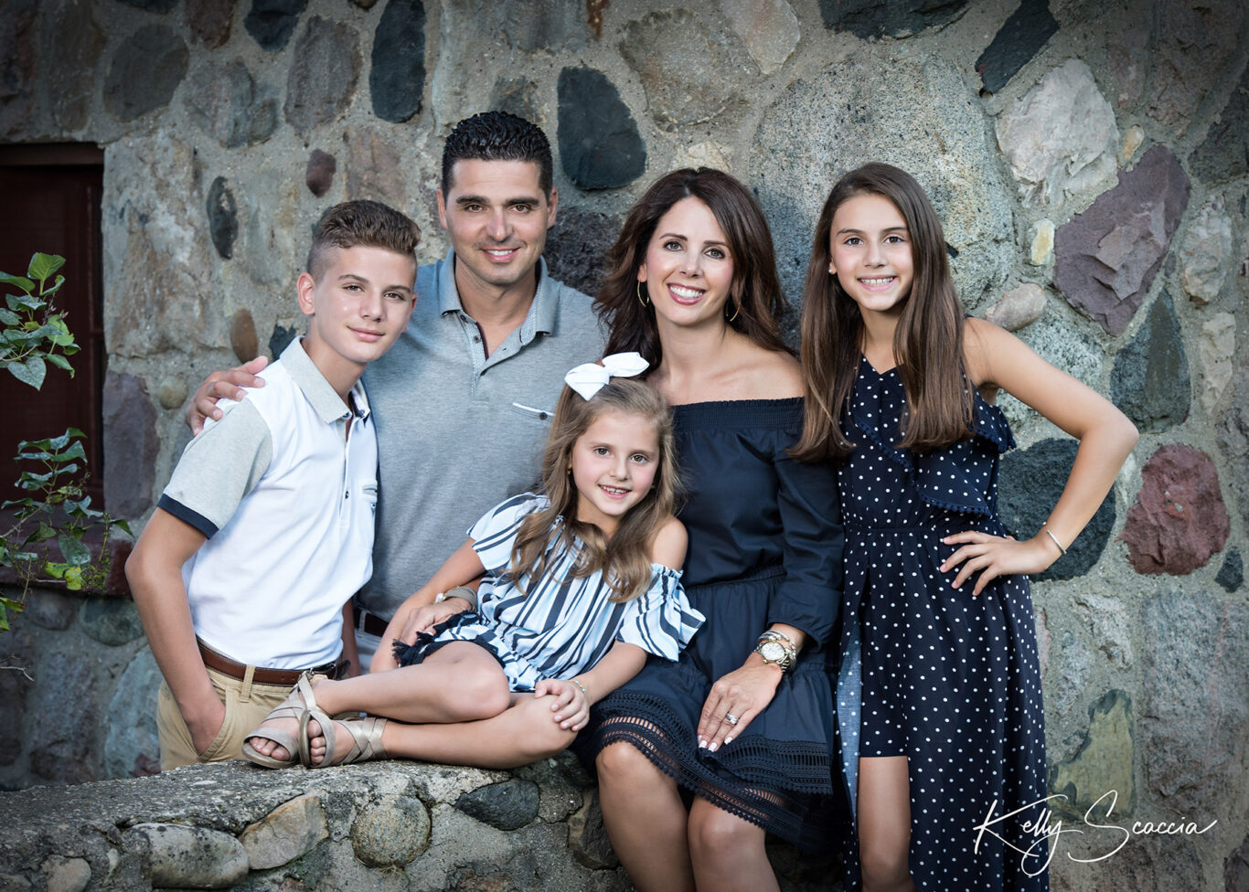 Family of five portrait outdoor with brick background smiling and looking directly at you