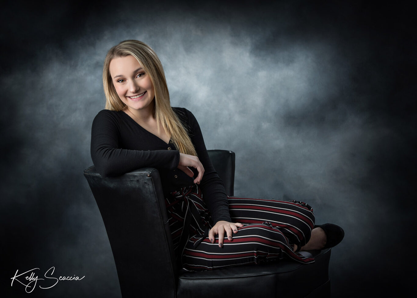 High School senior girl sitting in a chair in a studio portrait while smiling