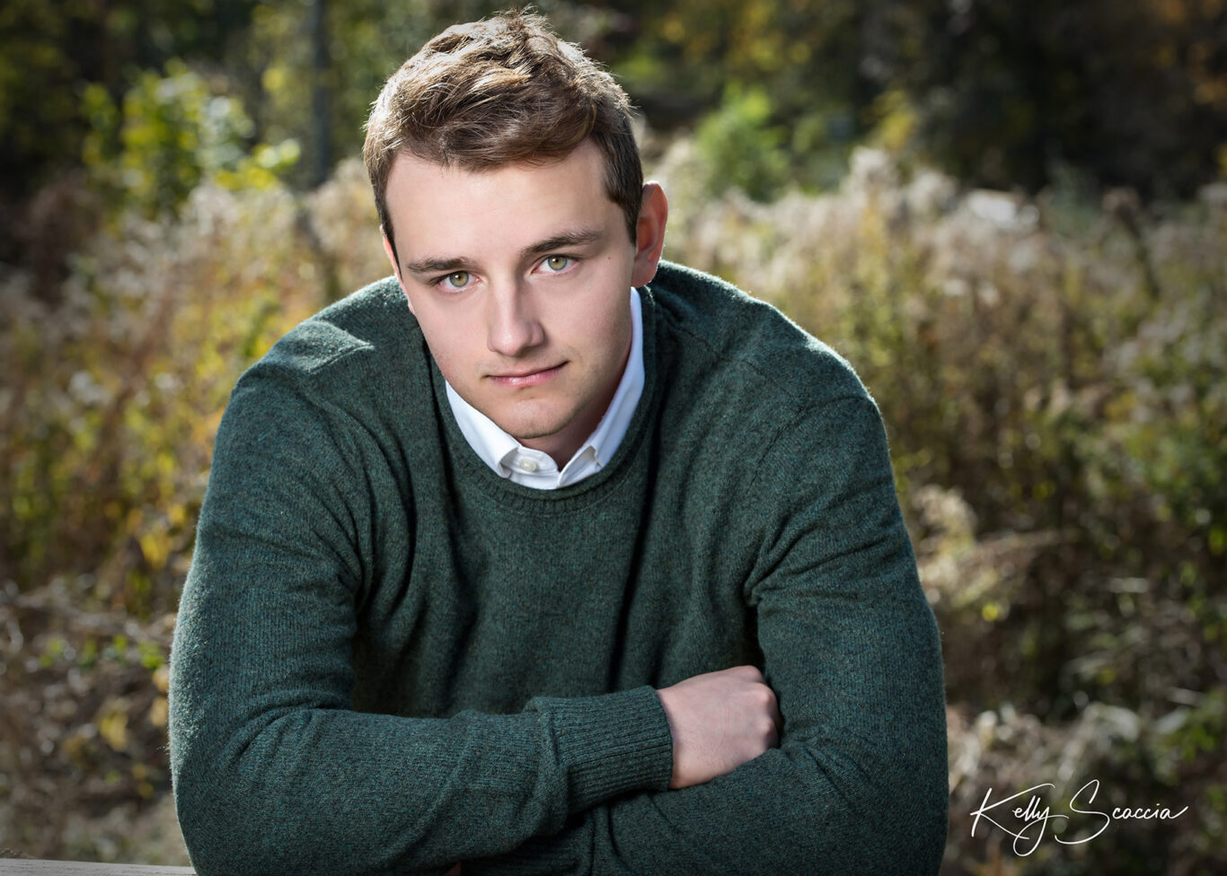 High School senior guy outdoor fall VanHoosen Farms Rochester Michigan leaning against the fence wearing a green sweater with arms crossed