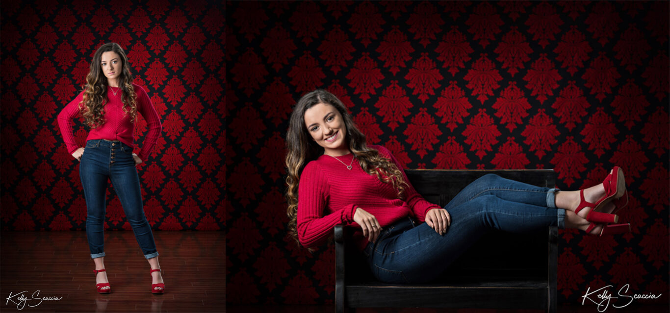 High School senior  girl in studio on a red damask background wearing a red sweater and jeans 