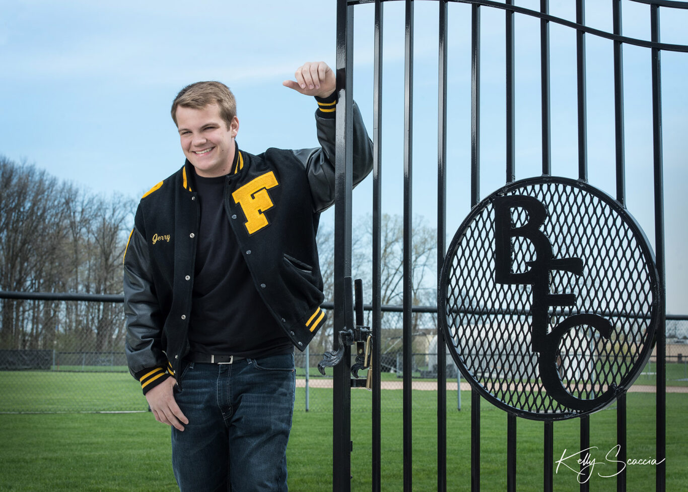 High School senior guy outdoor portrait in varsity jacket leaning against school iron fence Bishop Foley Catholic High School