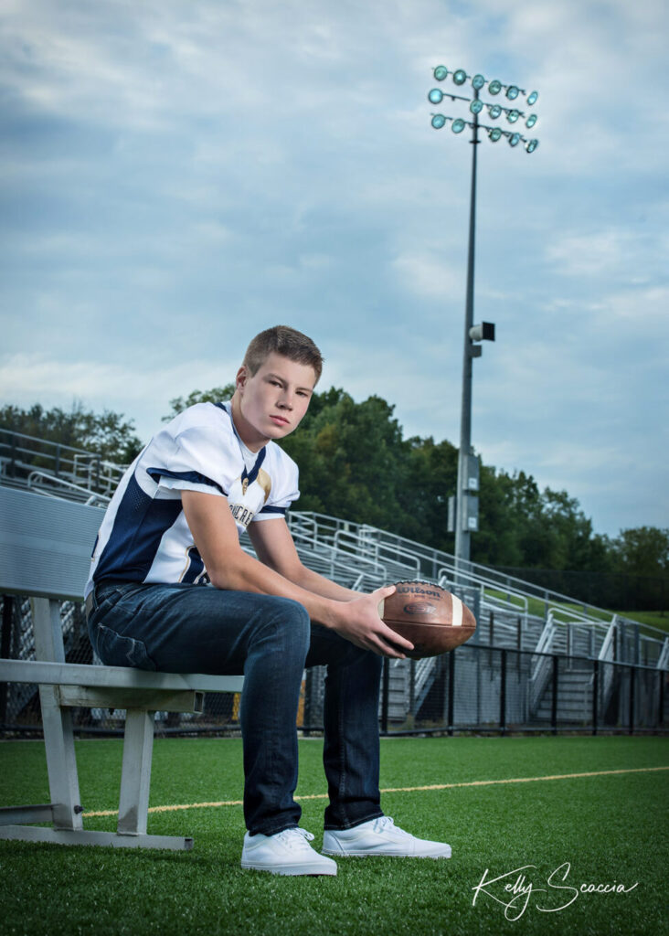 High School senior guy on a football field sitting on a bench holding a football Stoney Creek High School