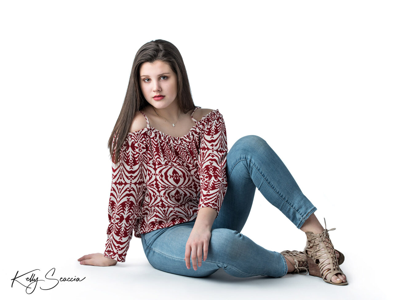 High School senior girl on white background sitting on hip with hand in lap looking directly at you