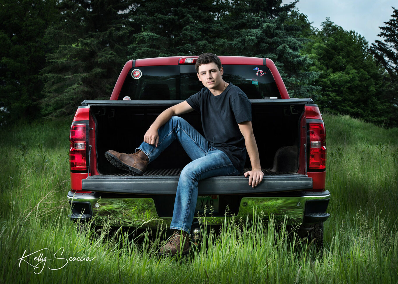 High School senior guy sitting on back of red pickup track with one let up and arm across his knee