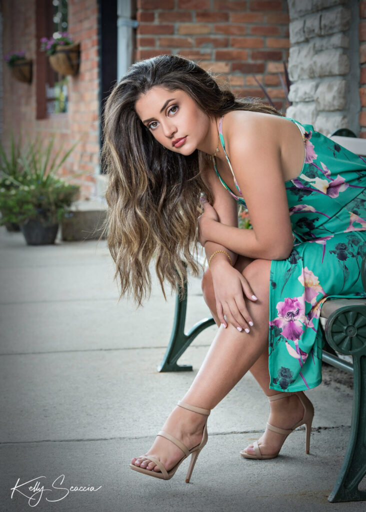High School senior girl Downtown Lake Orion wearing a green dress leaning forward on a bench with her hair draped over the side of her face
